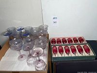 Two boxes holding twelve cranberry cut-to-clear wine glasses and a box of etched goblets visible