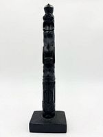 Full view of carved black stone totem pole standing on square base