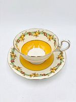 Teacup nested on saucer, showing interior yellow band and floral border