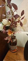 Full view of brown ceramic vase with faux arrangement on orange saucer