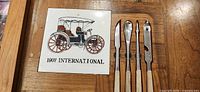 Close-up of tile showing vintage car and four stainless knives on oak board