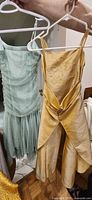 Front view showing both gold satin and mint tulle dresses on hangers