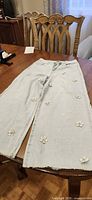 Full front view of light blue wide-leg jeans laid flat showing floral appliques and raw hems