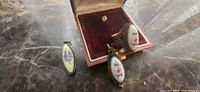 Ring in open red jewel box beside two elongated enamel drops on marble surface