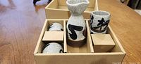 Box interior showing crackle-glaze carafe and cups in compartments