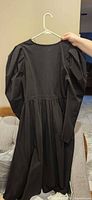 Back view of black midi dress on hanger showing puff sleeves and gathered skirt