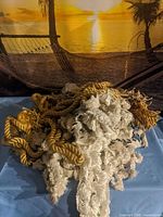 Pile of gold rope tiebacks and ivory fringe trim on blue surface