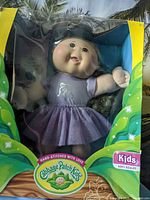 Front view of boxed Cabbage Patch Kids soft sculpt doll in purple dress