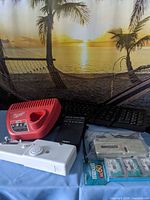 Overall view of all items on table: charger, radio, keyboards, sewing machine, cassette player, Maxell tapes