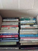 Overview of box containing assorted paperback books, spines visible
