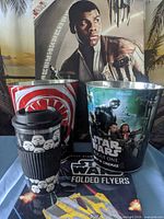Group shot of both metal popcorn buckets, stormtrooper tumbler, Folded Flyers book and Finn canvas wall art