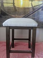 dark brown wood stool with light gray upholstered seat, full view