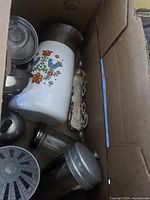Box view showing ceramic floral canister, silver utensil, glass jar and other metal items