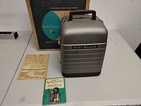 Projector case closed with manuals, power cord and original box visible