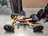 Full side view of orange BERG Buddy pedal go-kart showing frame, wheels, and steering wheel
