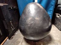 Full view of bulbous matte black ceramic vase resting on floor