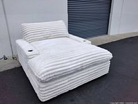 Angled view of white plush chaise lounge chair showing ribbed upholstery and overall structure