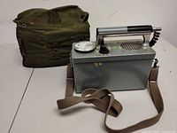 Geiger counter with strap alongside green canvas US-marked carry bag
