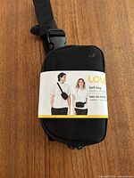 Front view of black Lolë belt bag with retail sleeve