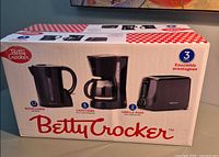 Front of sealed retail box showing images and descriptions of kettle, coffee maker, toaster