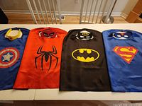 Four superhero capes laid flat with masks/tiara above each