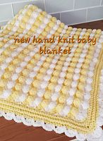 Folded yellow and white bobble-stitch baby blanket with scalloped edge