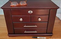 Front view of wooden jewelry box with drawers closed, glasses and marker for scale
