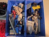 Close-up of blue sorting bin showing mixed blue, grey and white Lego pieces with unique parts like cockpit halves and wheels