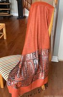 Full view of orange pashmina shawl draped over chair showing size and fringe