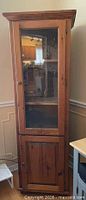 Front view of tall pine cabinet showing glass door, shelves, and lower door