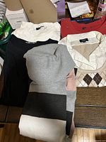 Stack of five tops showing ivory, black with white collar, colour-block, beige argyle Reitmans, red with grommets