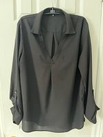 Front view of black draped blouse on hanger