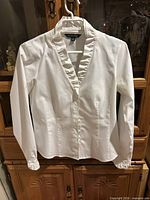 Front view of white ruffled Brooks Brothers blouse on hanger