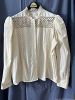 Front view of cream blouse on hanger showing lace insets, button front, long sleeves