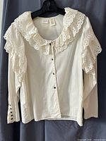 Front view of off-white blouse showing ruffled collar, shoulder lace, button front