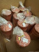 Box containing multiple cellophane-wrapped terracotta and gold pillar candles