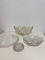 Four glass pieces on tabletop: footed bowl, oval ribbed dish, scalloped bowl, tealight holder