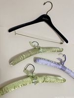 Black Neiman Marcus wooden hanger with metal bar and three satin padded hangers in light green and lavender