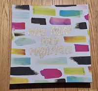 Front of square canvas showing colourful brushstrokes and gold glitter text