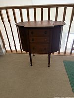 Front view showing sewing cabinet, drawers, turned legs, drop-leaf top