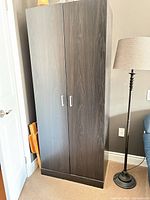Full exterior view of black two-door wardrobe beside lamp
