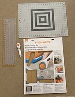 Grey cutting mat, clear acrylic ruler, rotary cutter, Fiskars boxed set shown