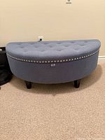 Full view of blue semicircular storage bench showing tufted seat, nailhead trim, and legs