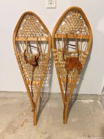Full view of both wooden snowshoes leaning against wall