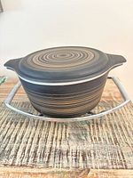 Casserole with lid seated in metal stand showing stripe pattern