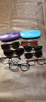 Eight pairs of assorted prescription eyeglasses and sunglasses with two hard cases displayed on surface