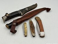 Group view of two fixed-blade knives in sheaths and three folding knives
