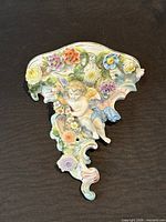 Front view of porcelain wall bracket showing cherub, scroll base, floral appliqués