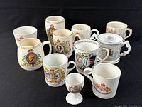 Group view of eleven commemorative mugs and small cup on black backdrop