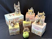 Group view of seven David Winter buildings with five original boxes and size reference apple